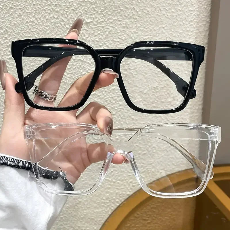 Una mano sostiene un par de gafas cuadradas negras y un par de gafas rectangulares transparentes.