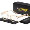 A pair of clear acetate eyeglasses with gold accents displayed next to a black box and a folded black cloth.