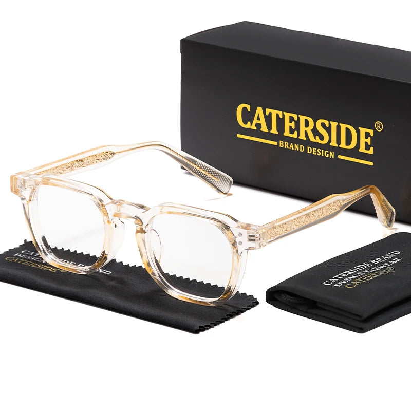 A pair of clear acetate eyeglasses with gold accents displayed next to a black box and a folded black cloth.