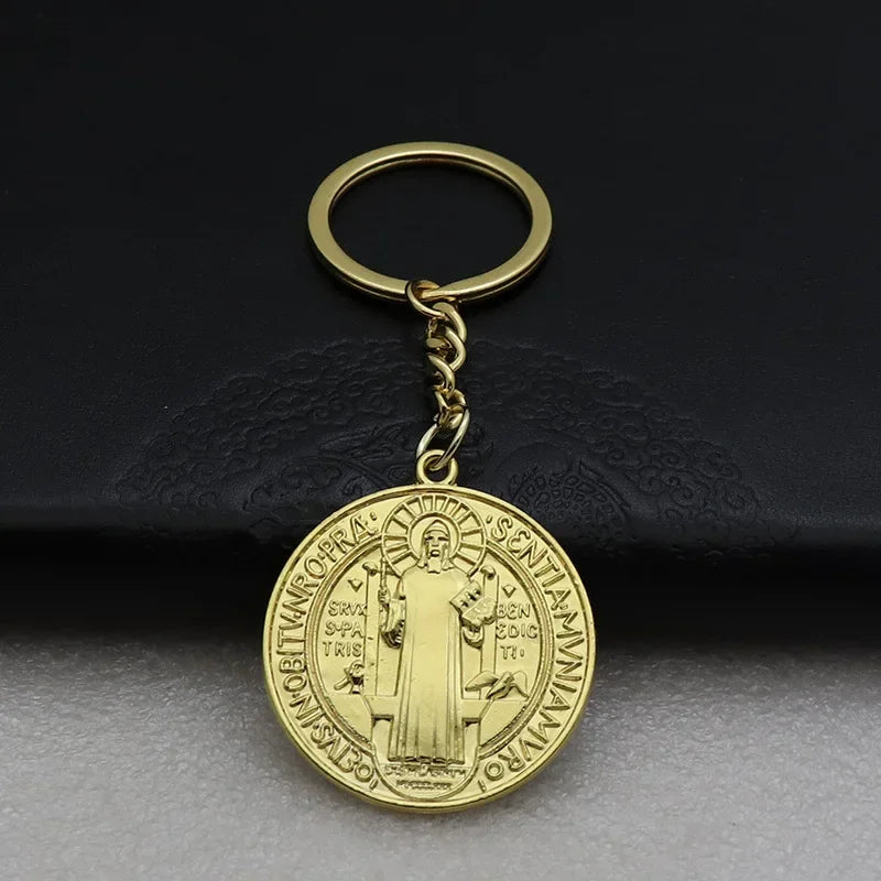 A round gold medallion keychain with a loop and chain, featuring an image of St. Benedict.