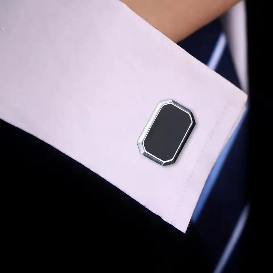 Pince-cuffs carrés argentés avec une pierre sombre sur une manche de chemise blanche.