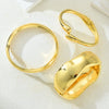 A set of three gold geometric wave bangles displayed on a white surface.