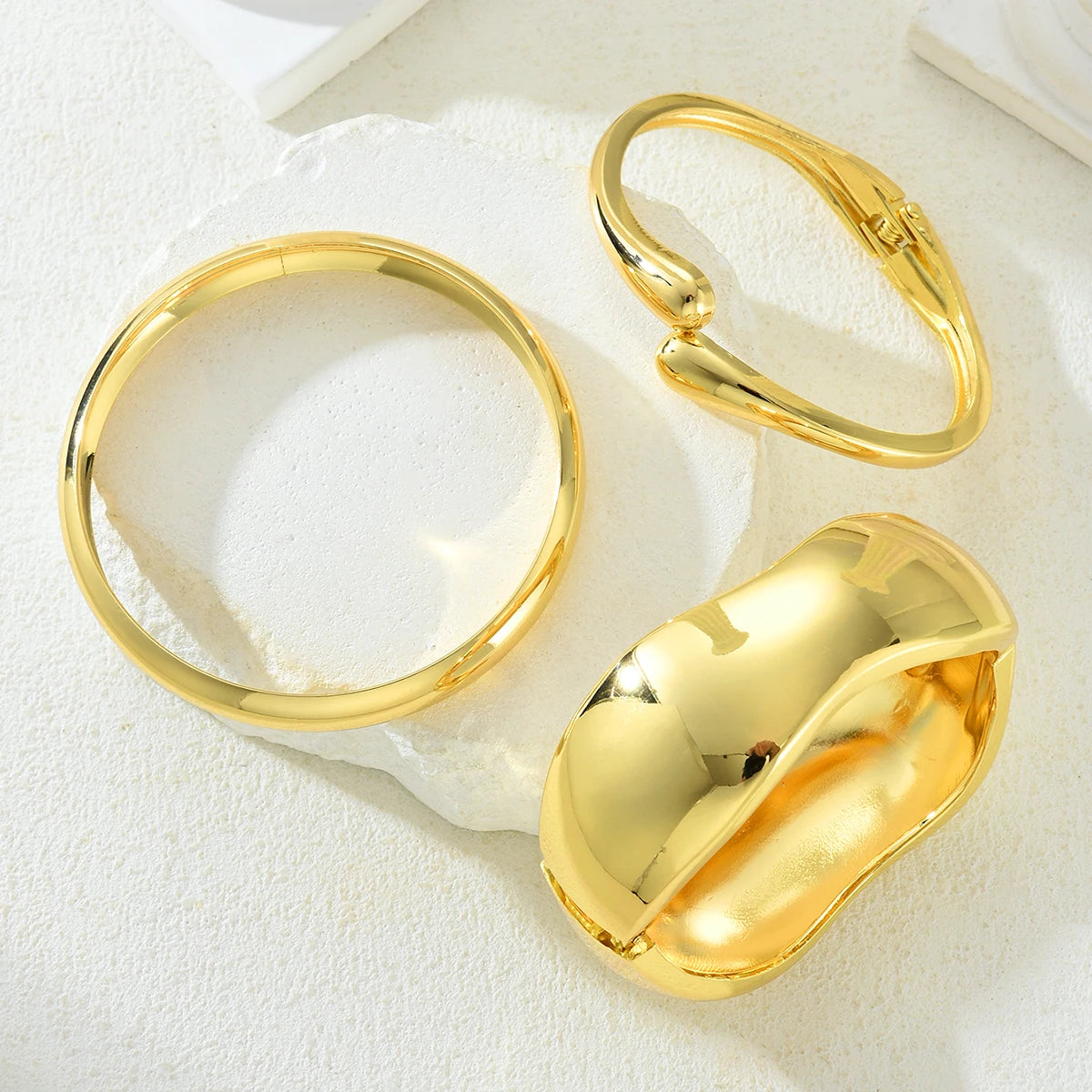 A set of three gold geometric wave bangles displayed on a white surface.