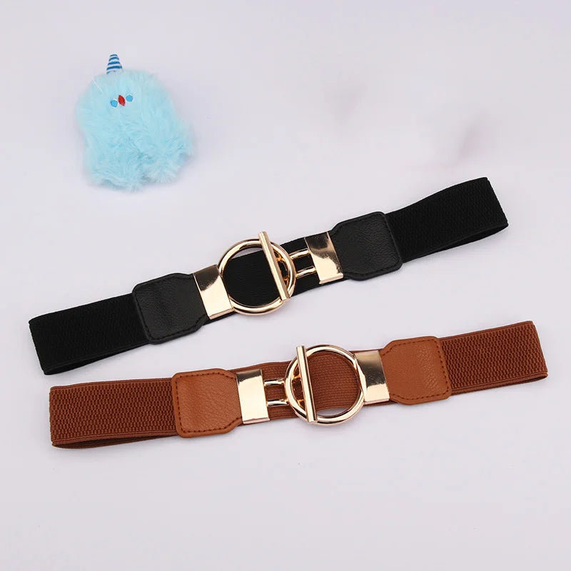 A black adjustable fashion belt with a gold buckle and a brown adjustable belt is shown next to a light blue fluffy toy.