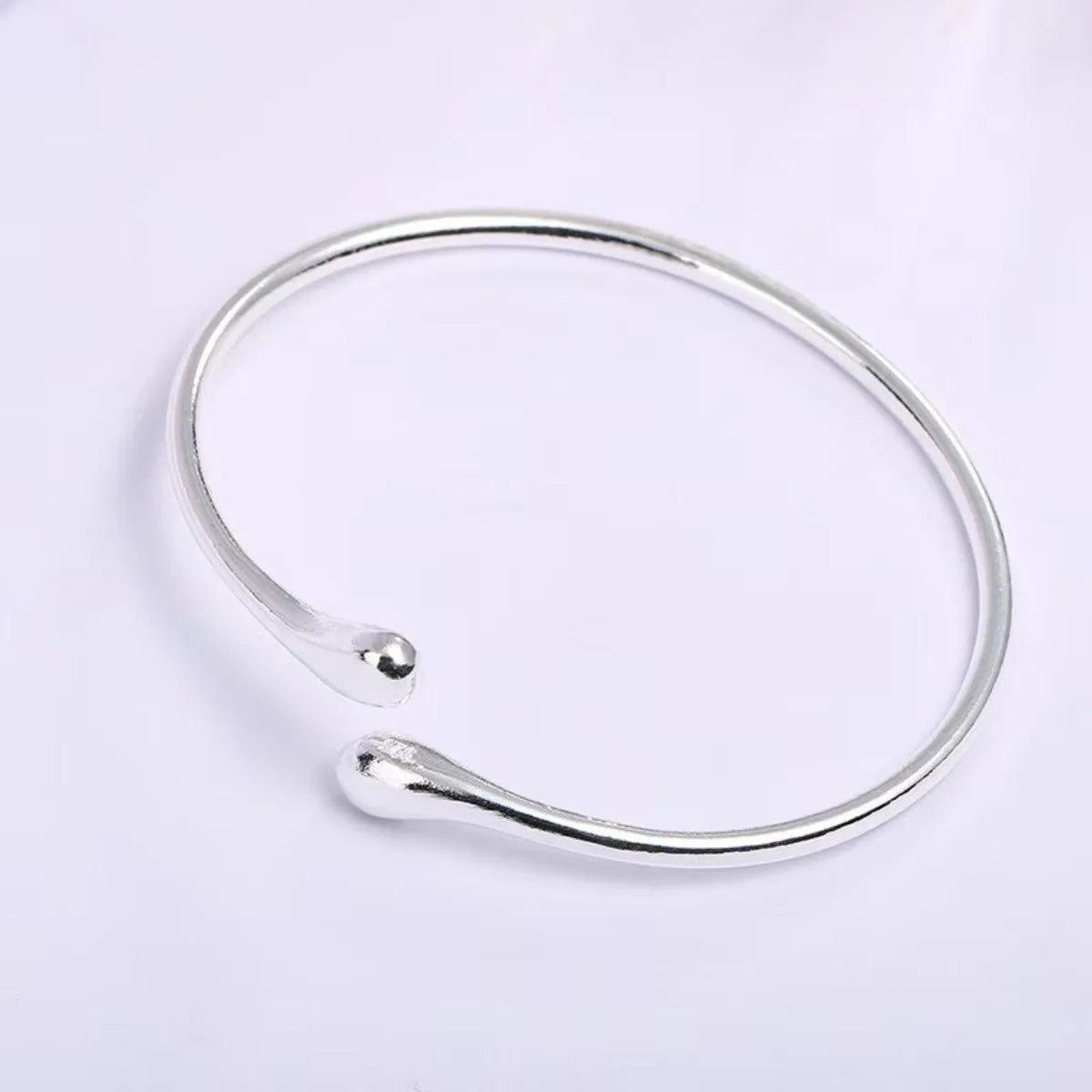 A silver adjustable stainless steel bangle with a droplet design shown against a white background.
