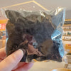 A hand holds a clear plastic bag filled with dark black elastic hair bands for girls.
