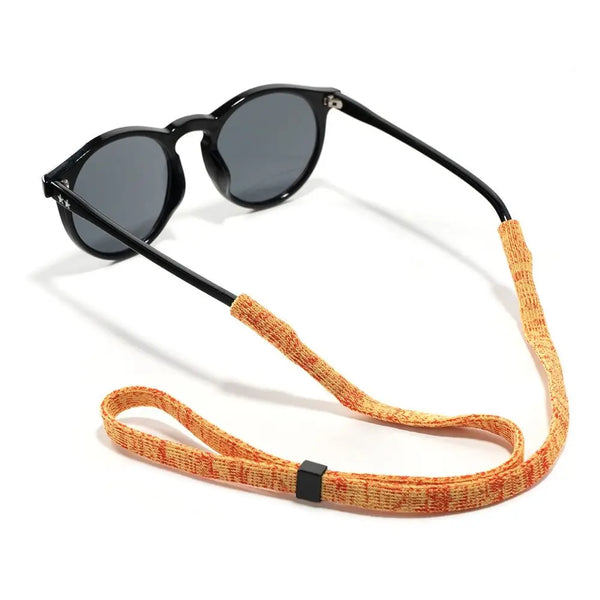 A pair of black sunglasses with an orange adjustable lanyard attached.