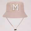 A light beige sun hat with a large gold letter M embroidered on the front.
