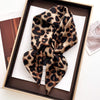 A luxury leopard print silk scarf tied in a bow displayed in a wooden box.