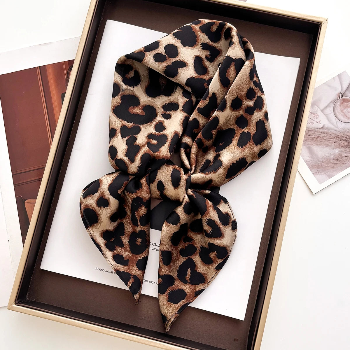 A luxury leopard print silk scarf tied in a bow displayed in a wooden box.