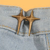 A pair of gold star-shaped decorative buttons fastened onto light blue denim fabric.