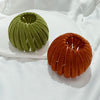 A green, textured horsetail hair clip is displayed on a white plate.
