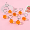 A set of orange, star-shaped anime keychains and a clear glass ring holder are displayed on a pink background.