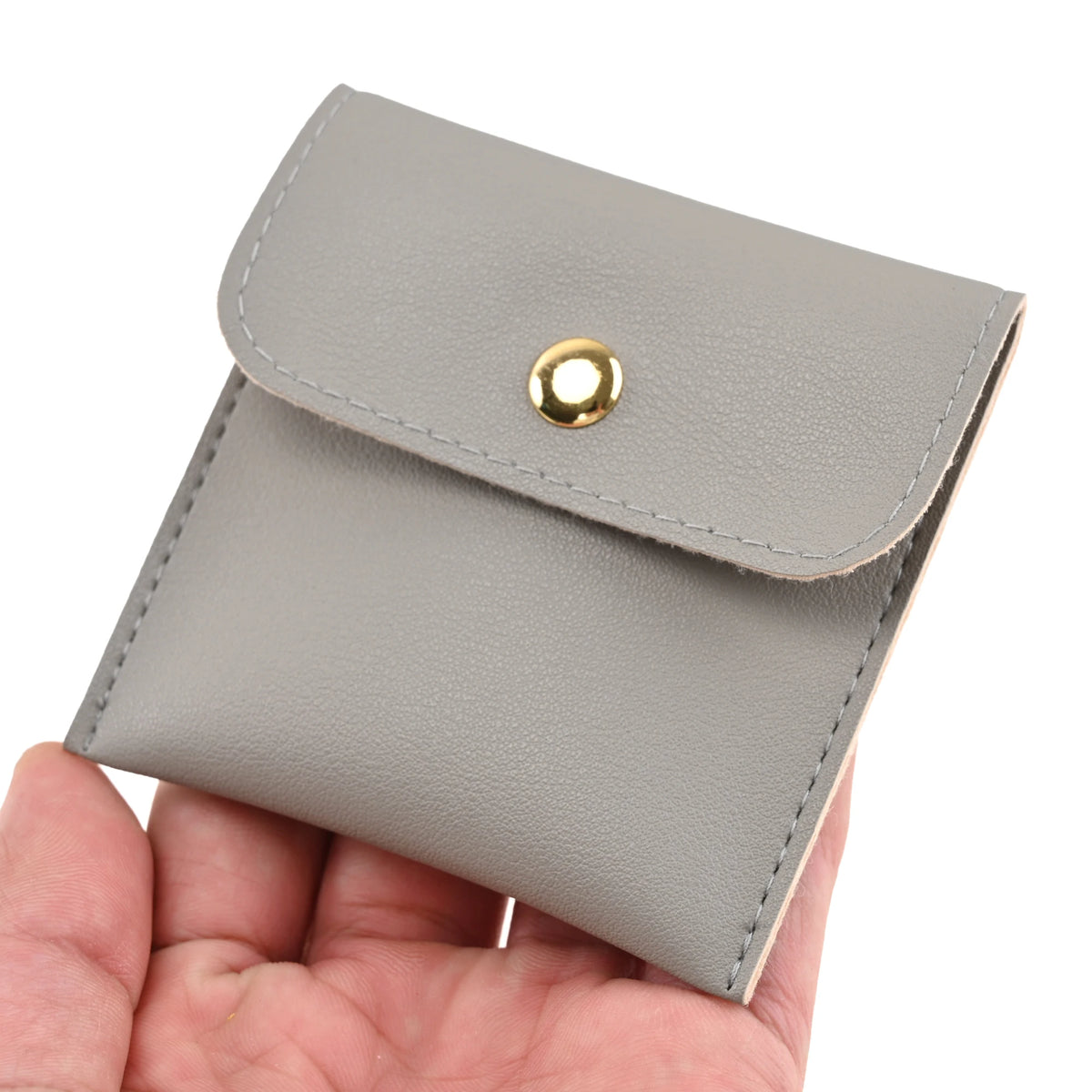 A gray PU leather jewelry pouch with a gold snap button being held in a hand.