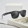 A pair of black vision correction pinhole glasses resting on a white box and a book.