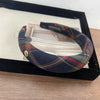 A black plaid sponge headband is displayed in a black frame on a wooden surface.