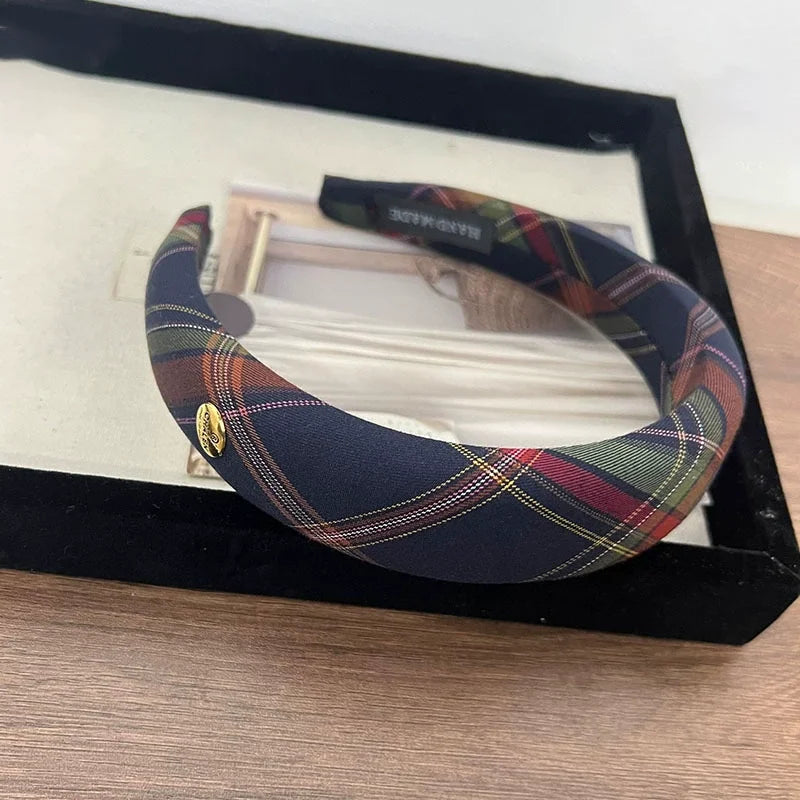 A black plaid sponge headband is displayed in a black frame on a wooden surface.
