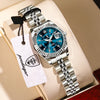 A silver wristwatch with a blue face and black bezel is displayed on a light-colored box.