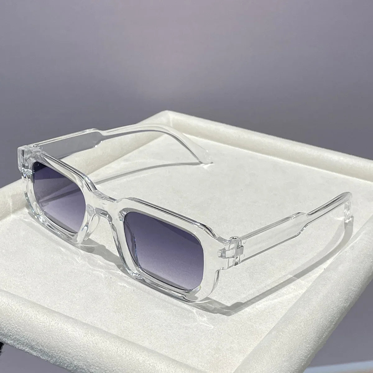 Clear plastic retro square sunglasses with purple lenses resting in a white box.