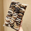 A bundle of solid color elastic hair ties in shades of brown and beige is shown packaged in clear plastic.