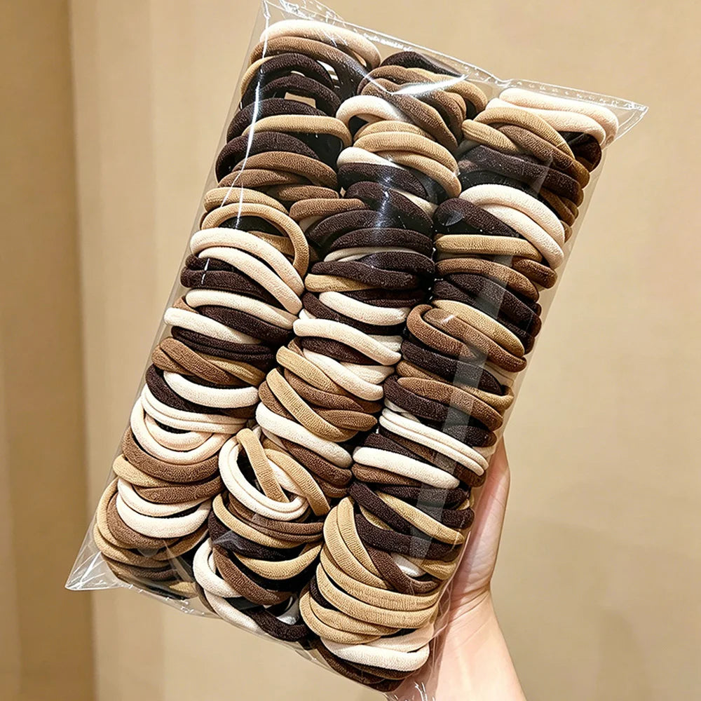 A bundle of solid color elastic hair ties in shades of brown and beige is shown packaged in clear plastic.