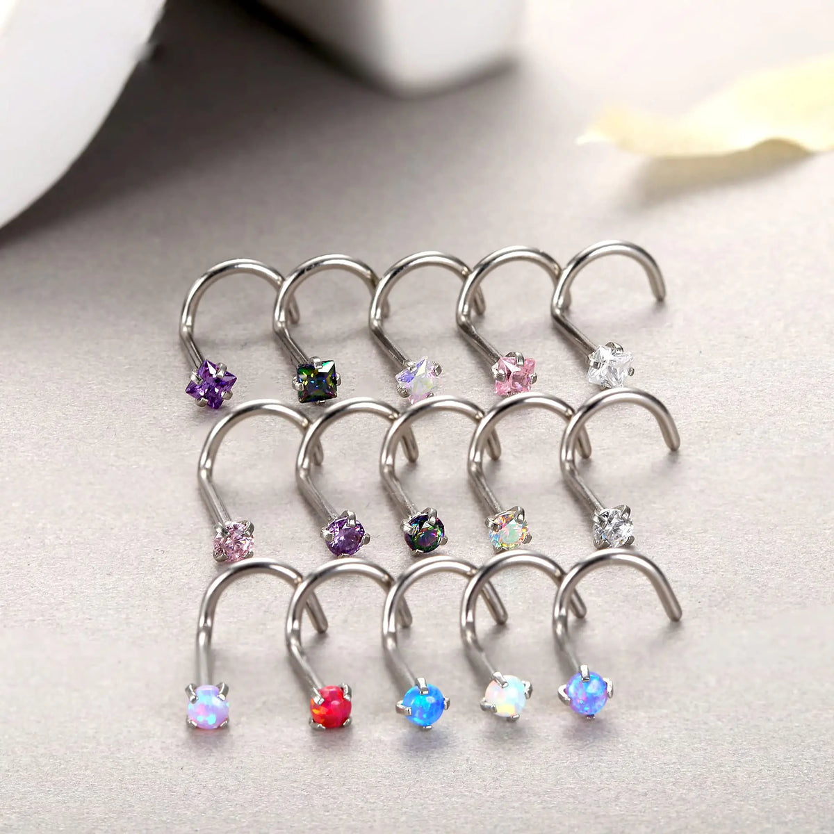 A collection of surgical stainless steel nose piercing studs featuring various colored and clear gemstones.