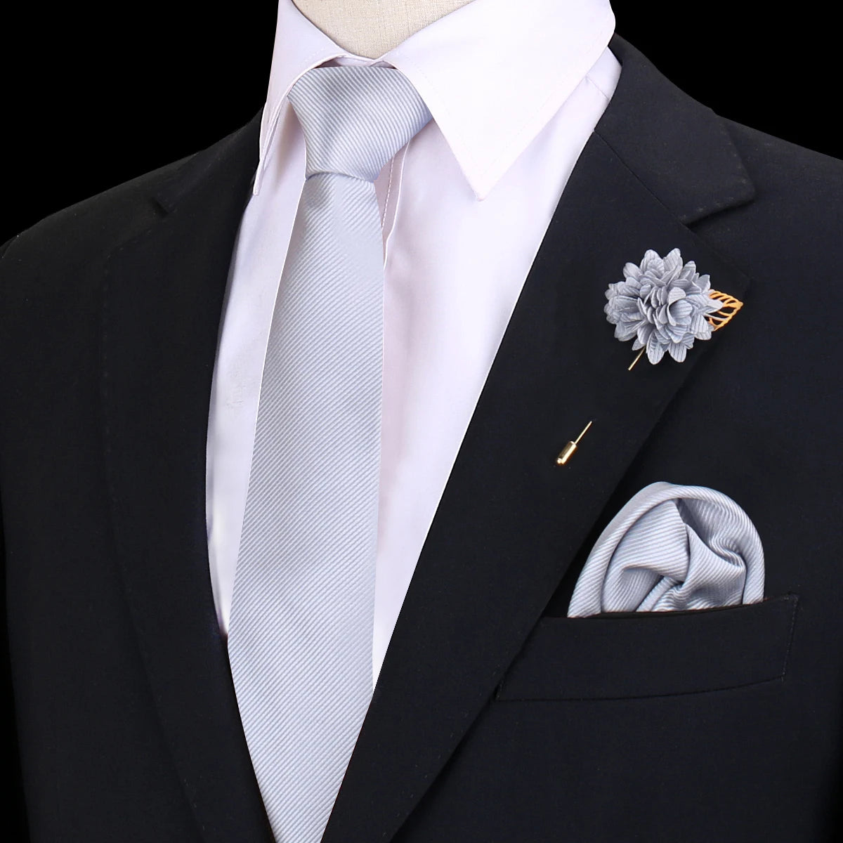 Chaqueta negra con camisa blanca, corbata azul claro a rayas y un prendido floral gris en la solapa.