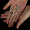 A hand holds a piece of jewelry featuring multiple small, oval connectors set with colored stones like red, blue, and gold.