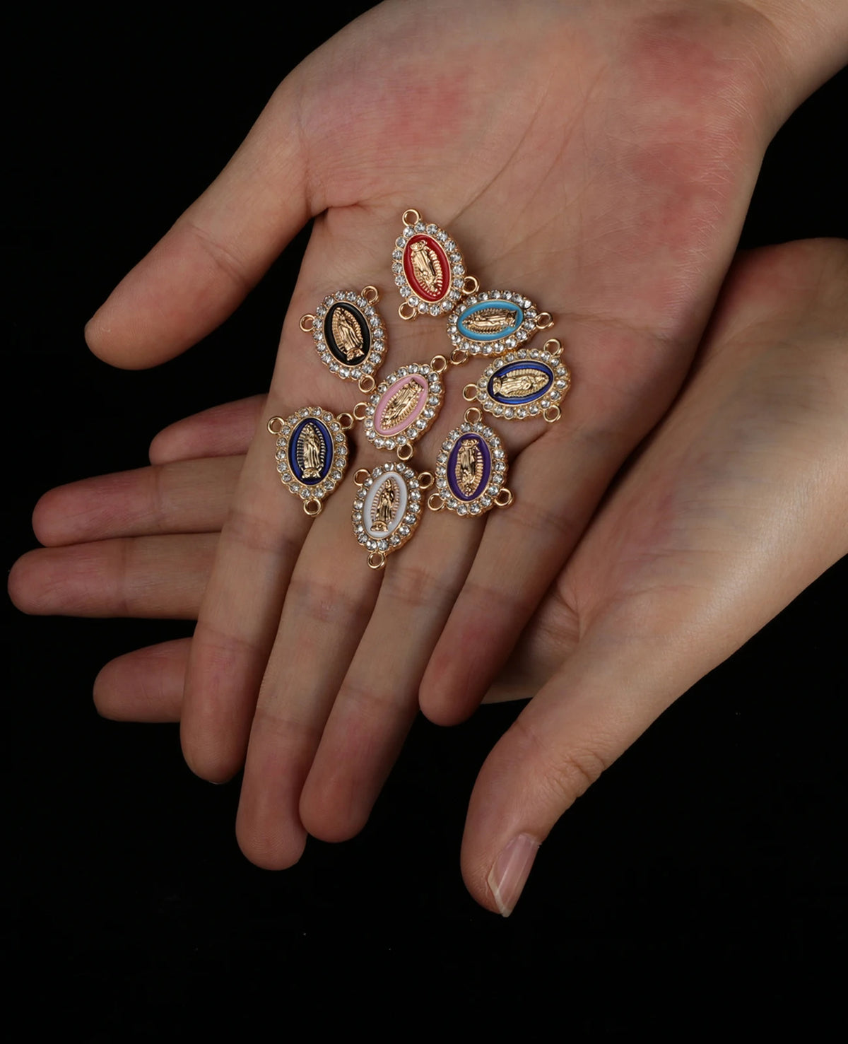 A hand holds a piece of jewelry featuring multiple small, oval connectors set with colored stones like red, blue, and gold.