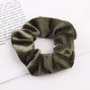 A close-up shot of a dark olive green velvet scrunchie, showing its textured fabric and gathered design.