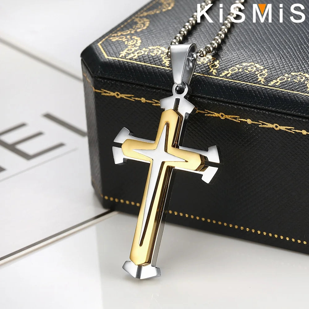 Colgante de cruz de acero inoxidable con detalles dorados, exhibido en una caja negra.