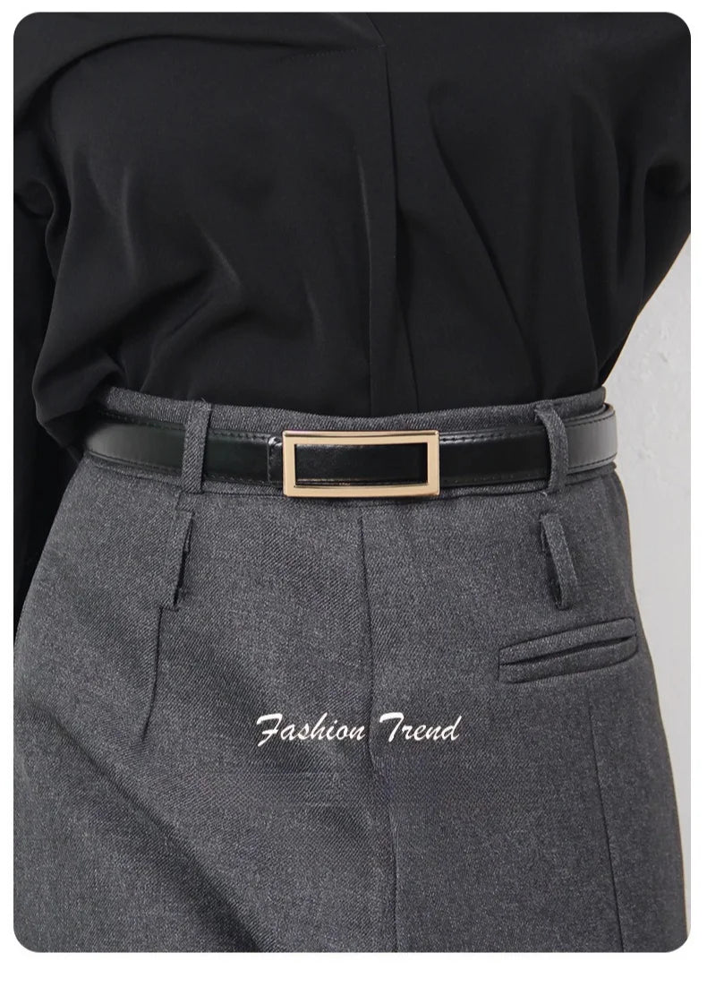 A close-up of a woman wearing a gray tailored skirt and a black belt with a gold buckle.