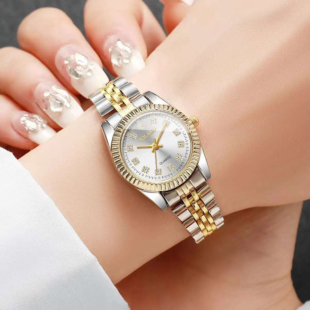 A close-up of a silver and gold rhinestone quartz wristwatch worn on a woman's wrist.