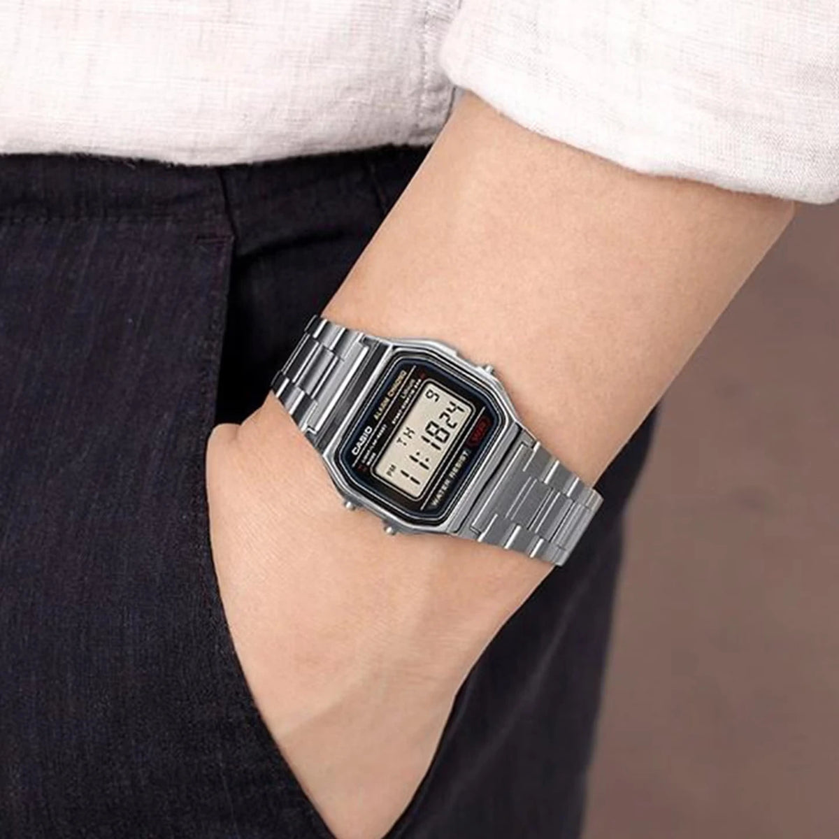 A close-up of a silver digital wristwatch with a black face and dark gray strap worn on a wrist.