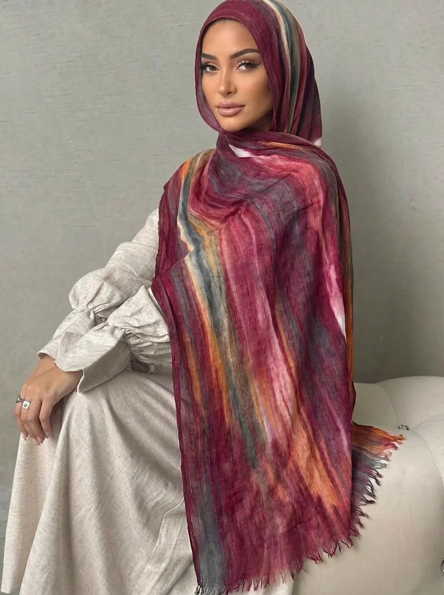 Una mujer vistiendo un pañuelo de hijab fluido, multicolor en tonos granate y púrpura