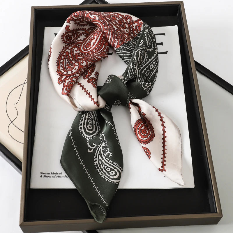 A luxury silk scarf featuring intricate paisley patterns in red, black, and cream colors displayed in a dark wooden frame.