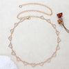 Gold-toned heart chain body jewelry with small clear stones laid out on a light background.