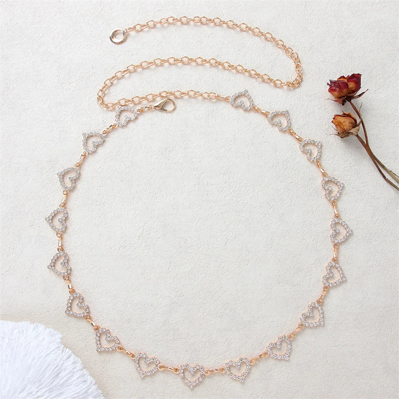 Gold-toned heart chain body jewelry with small clear stones laid out on a light background.