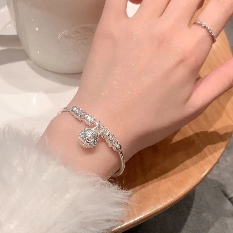 A close-up of a hand wearing silver bell bangles and a sparkling bracelet against a white background.