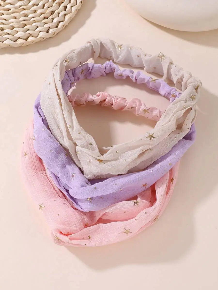 Ein Stapel von vier weichen Stoff-Haarbändern in Lavendel-, Rosa- und Weißtönen mit kleinen goldenen Stern-Prints.