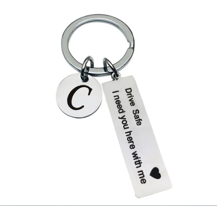 Silver keychain with a circular initial C and a tag that reads Drive Safe I need you here with me