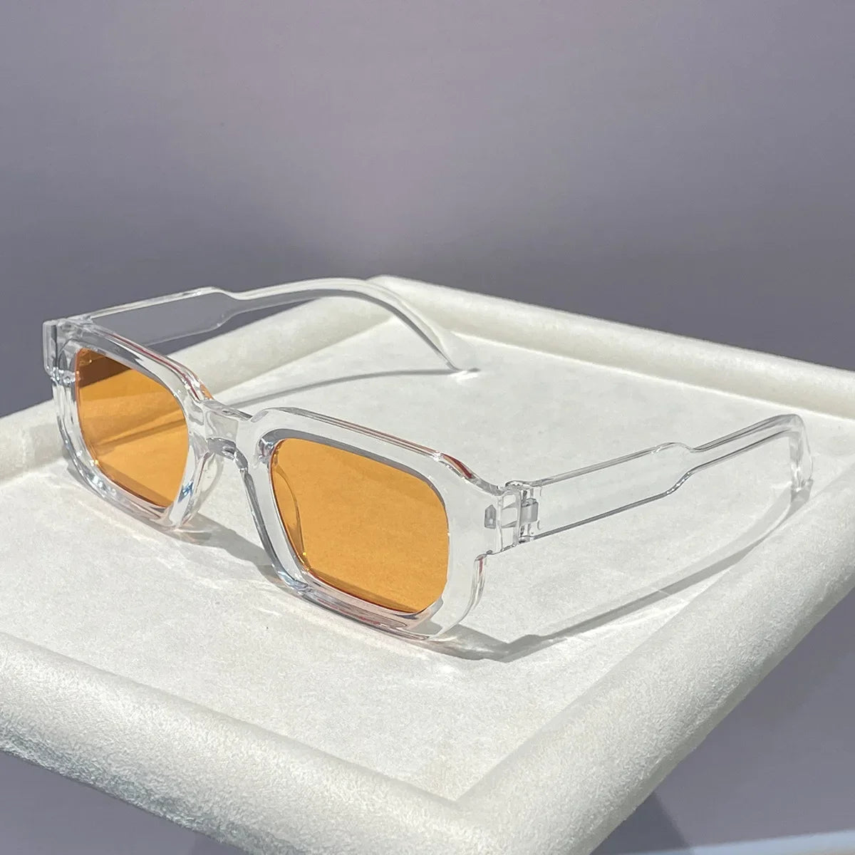 Clear plastic retro square sunglasses with orange lenses resting in a white box.