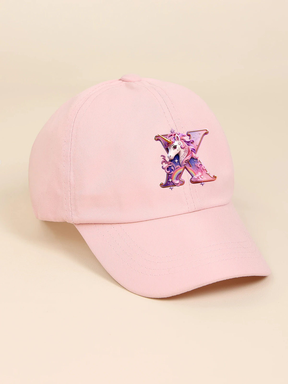 A pink baseball cap featuring a purple and iridescent unicorn letter design.
