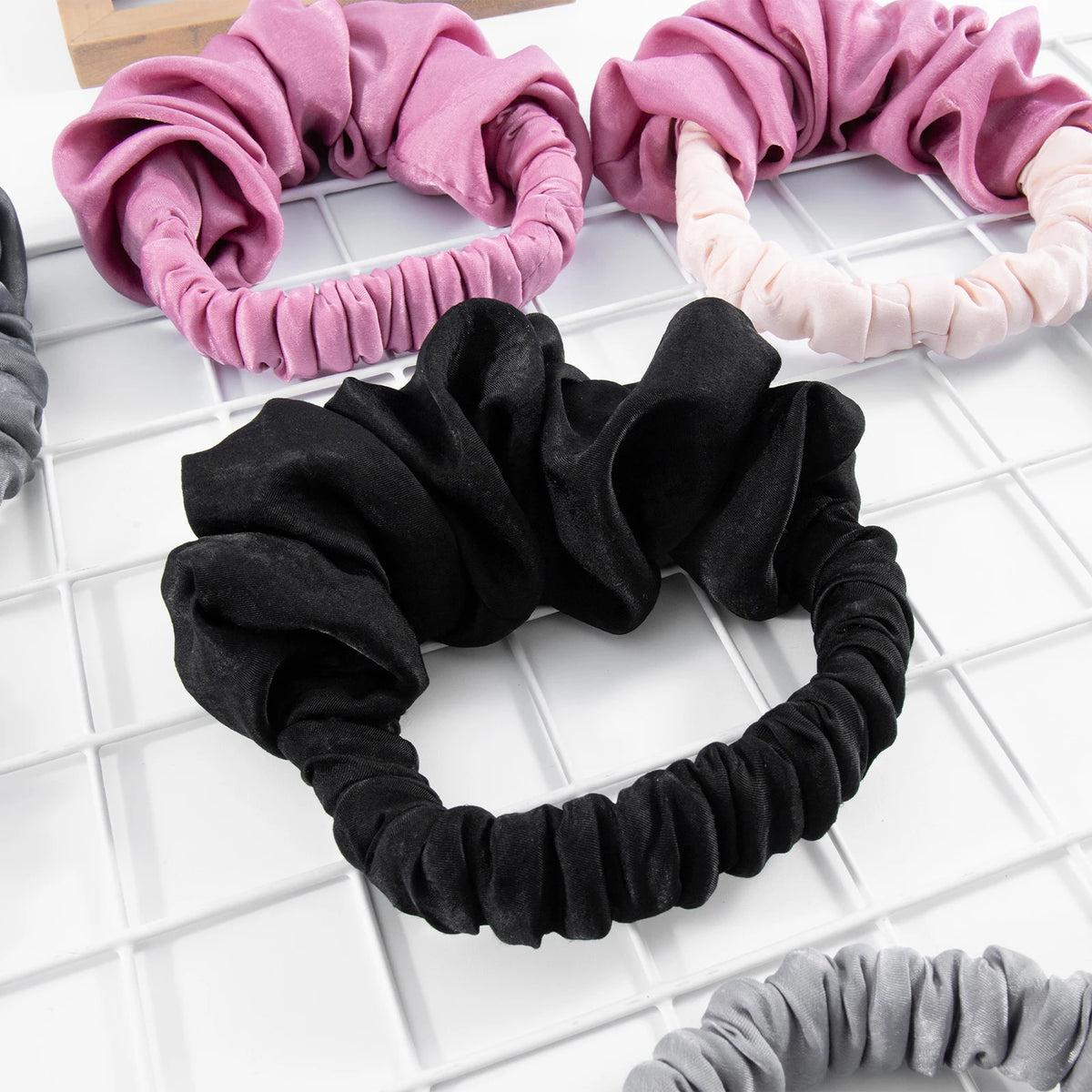 A collection of heatless hair curling scrunchies in shades of pink, black, and gray arranged on a white grid.