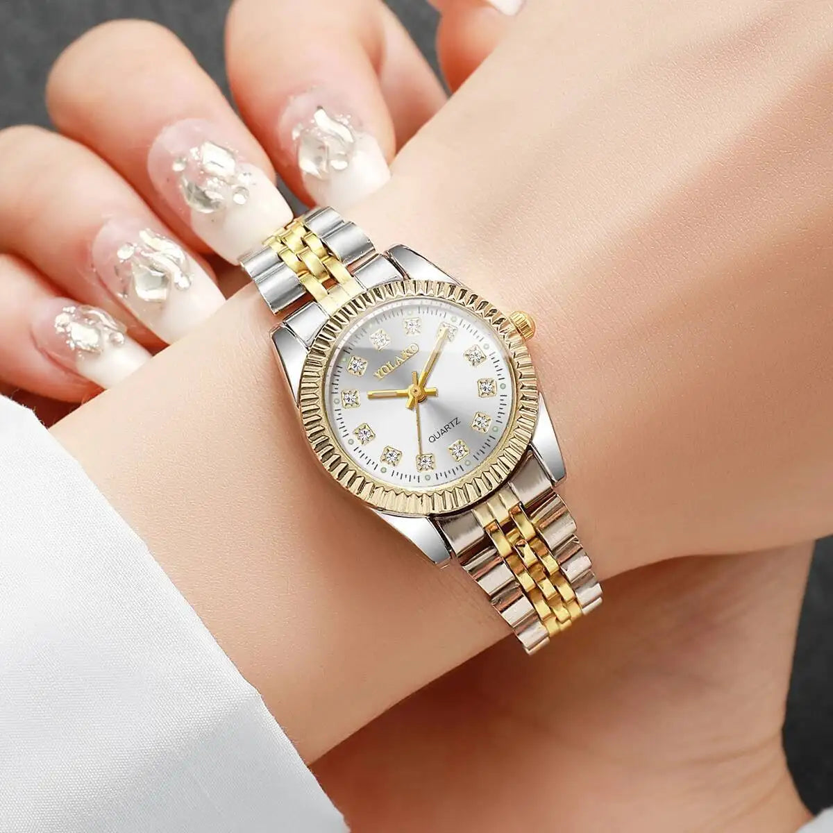 A close-up of a silver and gold rhinestone quartz wristwatch worn on a woman's wrist.