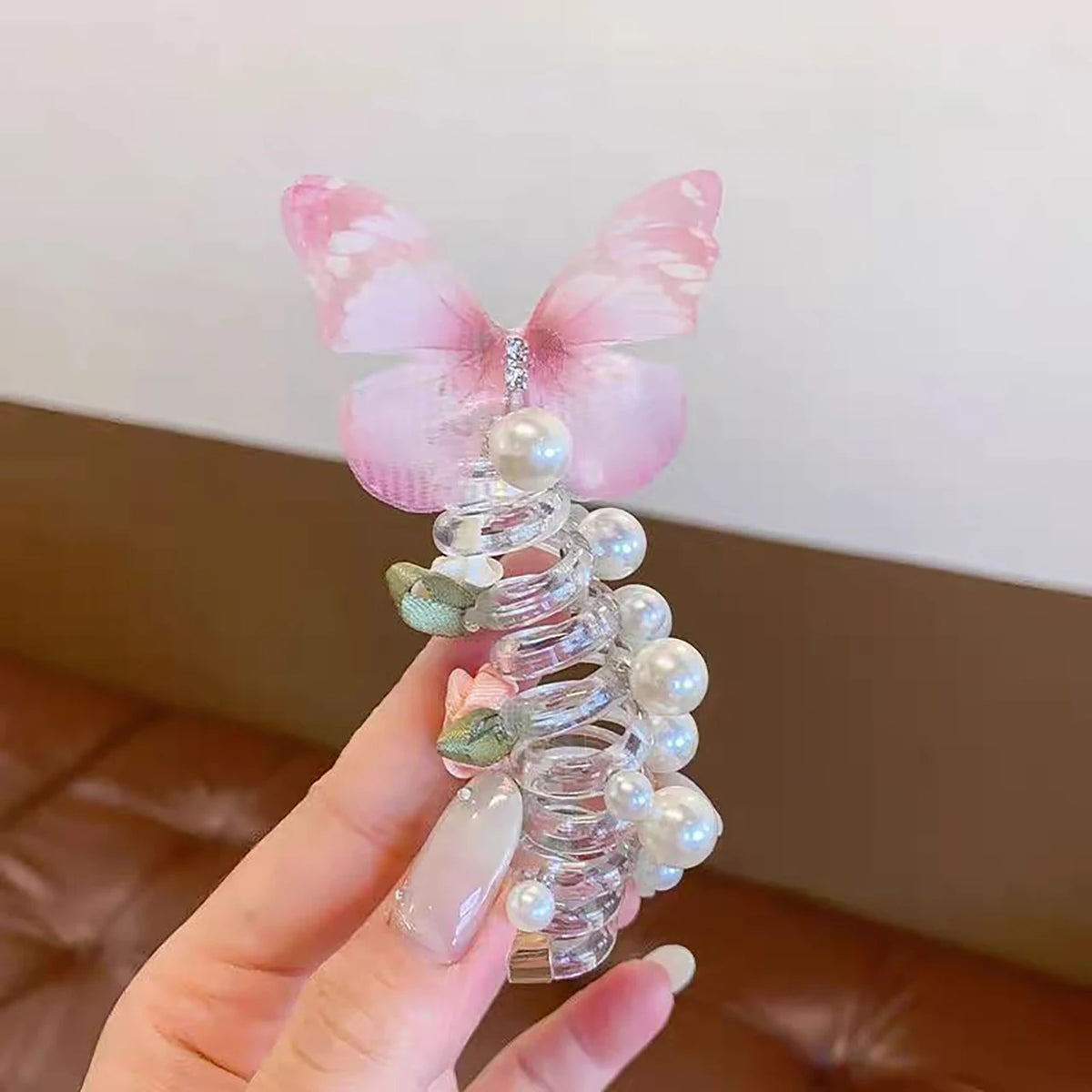 A pink fairy butterfly made of clear glass and pearl hair ropes held in a hand.