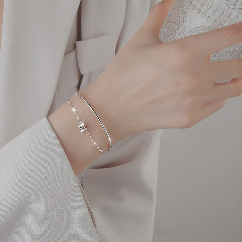 A close-up of a woman's wrist wearing a sterling silver double heart charm bracelet on a light gray suit sleeve.