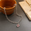 Silver chain necklace with a pink crystal heart pendant resting on a dark surface next to a ceramic cup and bread.