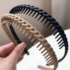A hand is holding a black braided hair headband and a beige braided hair headband.