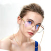 A woman wearing round, translucent pink-tinted eyeglasses with a gold chain lanyard.